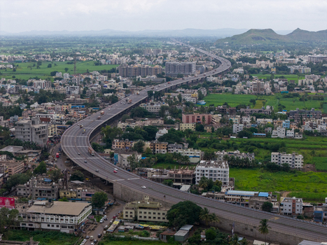 Aerial view of a highway winding through the town of Karad surrounded by residential buildings lush green fields and distant hills in Karad Maharashtra India.