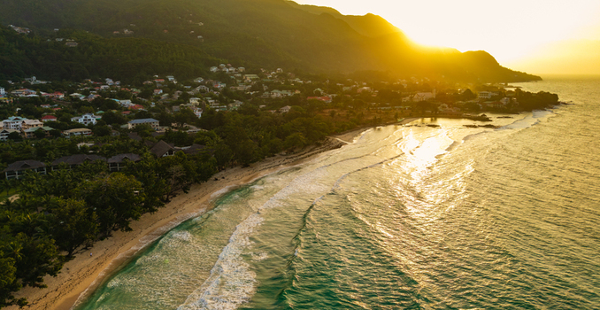 Aerial view of Anse Soleil Beachcomber Hotel along the lush coastline with golden sunset light reflecting on turquoise ocean waves and sandy beach in Mahe Baie Lazare Seychelles.