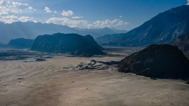 Aerial view of Sarfaranga Cold Desert Shigar with vast sand dunes rugged mountains and a winding river under a clear blue sky in Skardu Gilgit Pakistan.