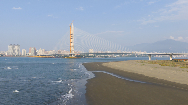 Aerial view of the Danjiang Bridge under construction spanning the Tamsui River with a sandy beach and city skyline in the background in Tamsui District New Taipei City Taiwan.