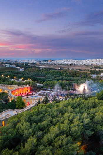 Aerial view of Park Nazzjonali Ta Qali with an evening event featuring illuminated structures and crowds amidst lush trees under a vibrant sunset sky in Attard Northern Region Malta. Aerial view of Park Nazzjonali Ta Qali with an evening event featuring illuminated structures and crowds amidst lush trees under a vibrant sunset sky in Attard Northern Region Malta.