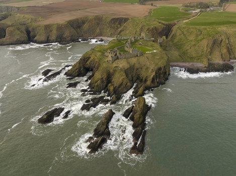 Aerial view of the medieval ruins of Dunnottar Castle perched on a rocky headland surrounded by the North Sea and steep cliffs in Stonehaven Scotland United Kingdom. Aerial view of the medieval ruins of Dunnottar Castle perched on a rocky headland surrounded by the North Sea and steep cliffs in Stonehaven Scotland United Kingdom.