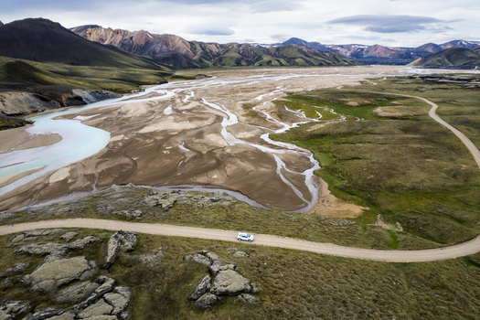 Aerial view of the F208 road with a white car driving through the volcanic landscape and braided glacial rivers of the Icelandic Highlands Iceland. Aerial view of the F208 road with a white car driving through the volcanic landscape and braided glacial rivers of the Icelandic Highlands Iceland.