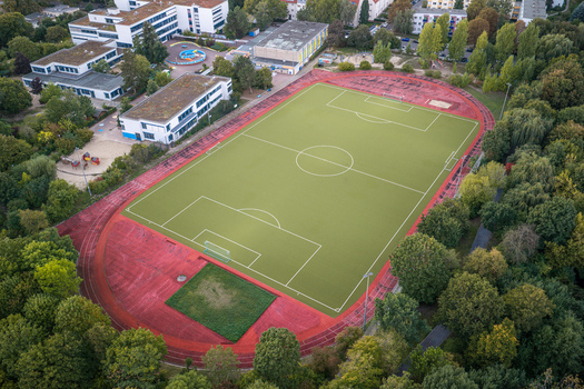 Aerial view of the High Deck Siedlung soccer field with a red running track surrounded by lush trees and residential buildings in Berlin Berlin Germany. Aerial view of the High Deck Siedlung soccer field with a red running track surrounded by lush trees and residential buildings in Berlin Berlin Germany.
