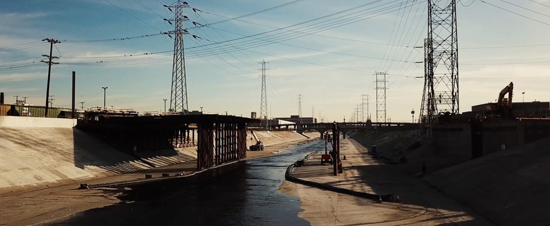 Aerial view of the Los Angeles River with concrete banks construction scaffolding and high voltage power lines under a clear sky in Los Angeles California United States.