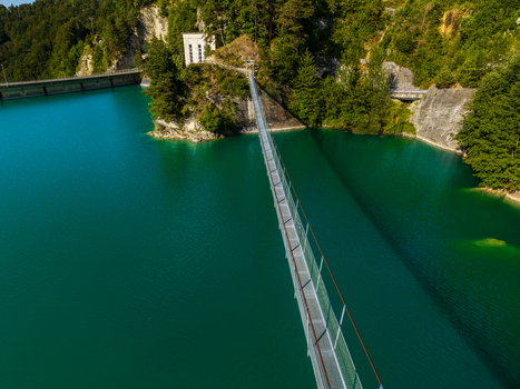 Aerial view of the suspension bridge over the turquoise waters of Lac de la Gruyere near the Barrage de Rossens surrounded by lush green forests in Pont la Ville Fribourg Switzerland.