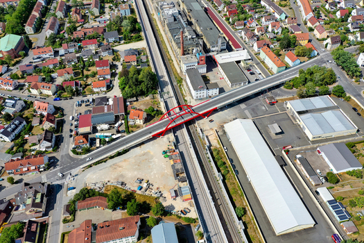 Aerial view of Piastenbrucke red arched bridge crossing over railway tracks and industrial buildings in Forchheim Bayern Germany.