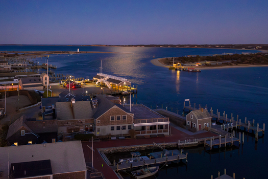 View of Martha s Vineyard harbor at twilight with illuminated waterfront buildings wooden docks and the distant lighthouse under a deep blue evening sky in Edgartown Massachusetts United States.