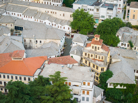 Aerial view of the historic old town featuring traditional stone roofed houses narrow cobblestone streets and lush green trees in Gjirokaster Gjirokaster County Albania. Aerial view of the historic old town featuring traditional stone roofed houses narrow cobblestone streets and lush green trees in Gjirokaster Gjirokaster County Albania.