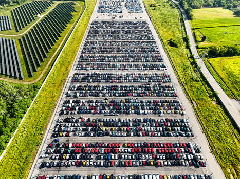 Aerial view of a massive car storage lot filled with rows of vehicles next to a large solar panel farm and green fields in Rivalta di Torino Piedmont Italy. Aerial view of a massive car storage lot filled with rows of vehicles next to a large solar panel farm and green fields in Rivalta di Torino Piedmont Italy.