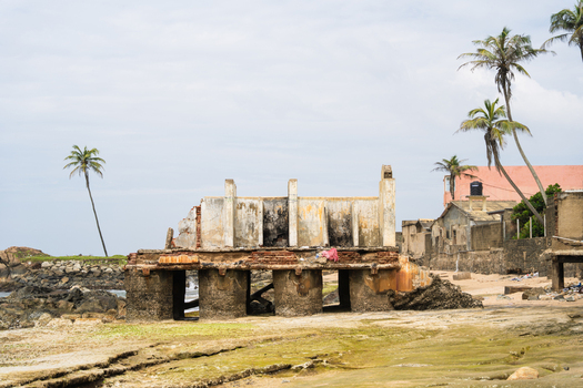 View of a ruined coastal building with weathered concrete walls and palm trees on a rocky beach in Galle Southern Province Sri Lanka.