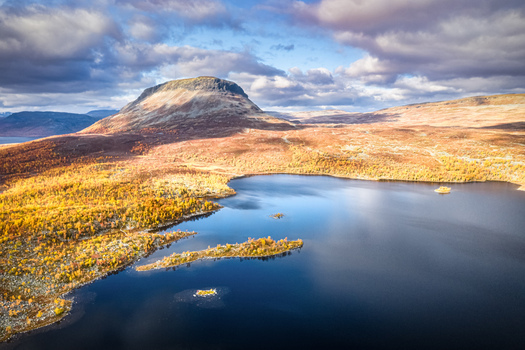 Aerial view of the iconic Saana fell rising above the deep blue waters of Lake Kilpisjarvi surrounded by vibrant autumn foliage under a dramatic cloudy sky in Kilpisjarvi Lapland Finland.
