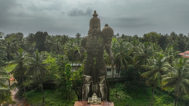 Aerial view of the large Hanuman statue surrounded by lush palm trees and greenery under a cloudy sky in Udupi Karnataka India. Aerial view of the large Hanuman statue surrounded by lush palm trees and greenery under a cloudy sky in Udupi Karnataka India.