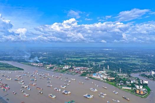 Aerial view of the Karnaphuli River filled with numerous cargo ships and barges with industrial facilities along the riverbank under a bright blue sky in Chattogram Chittagong Division Bangladesh.