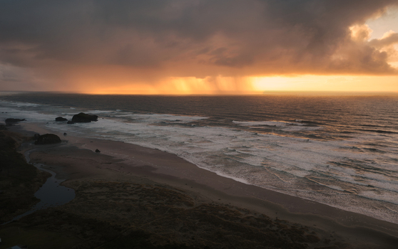 Aerial view of a dramatic winter storm over the Pacific Ocean coastline at sunset with rain shafts dark clouds and waves crashing on the beach in Bandon Oregon United States. Aerial view of a dramatic winter storm over the Pacific Ocean coastline at sunset with rain shafts dark clouds and waves crashing on the beach in Bandon Oregon United States.