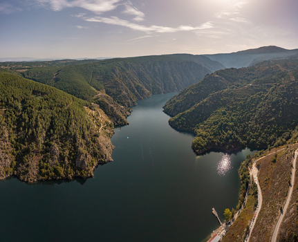 Aerial view of the Ribeira Sacra canyon with the Sil River winding through steep forested hills rocky cliffs and sunlight reflecting on the water in Lugo Ourense Spain. Aerial view of the Ribeira Sacra canyon with the Sil River winding through steep forested hills rocky cliffs and sunlight reflecting on the water in Lugo Ourense Spain.
