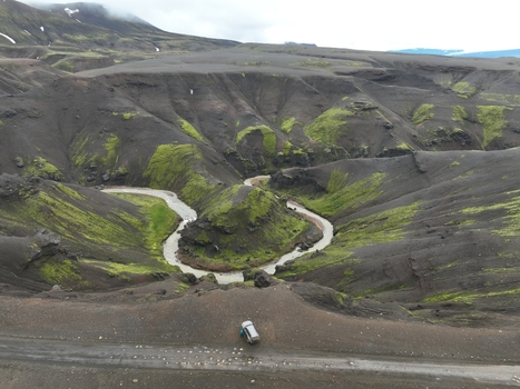 Aerial view of the winding river in the volcanic landscape of Kerlingarfjoll with mossy slopes and dark soil with a vehicle on a dirt road in Fludir Hrunamannahreppur Iceland. Aerial view of the winding river in the volcanic landscape of Kerlingarfjoll with mossy slopes and dark soil with a vehicle on a dirt road in Fludir Hrunamannahreppur Iceland.