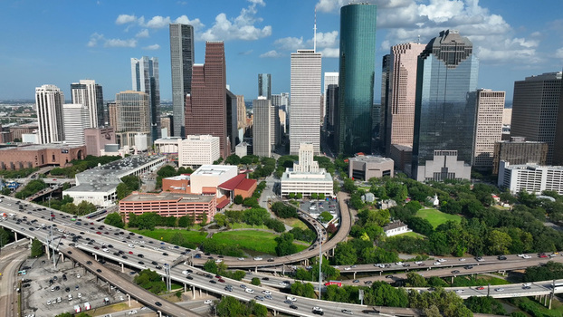 Aerial view of Houston skyline with modern skyscrapers glass office buildings and a busy highway interchange under a clear blue sky in Harris County Texas United States.
