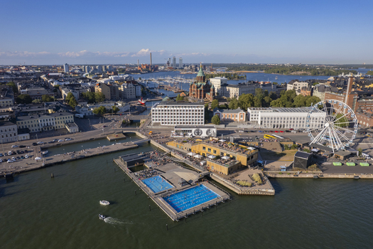 Aerial view of Allas Sea Pool with swimming pools the iconic Uspenski Cathedral a Ferris wheel and harbor boats in the urban landscape of Helsinki Uusimaa Finland.