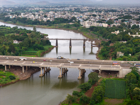 Aerial view of the Krishna River in Karad featuring a modern highway bridge and an historic stone bridge surrounded by lush green banks and the urban landscape of Karad Maharashtra India.