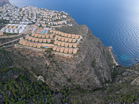 Aerial view of residential complexes with swimming pools on a rocky cliff overlooking the Mediterranean Sea surrounded by pine forests in Moraira Valencian Community Spain.
