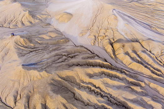 Aerial view of the Mud Volcanoes of Paclele Mari showing the unique cratered and cracked landscape with grey mud flows and two people standing on the terrain in Paclele Buzau County Romania.