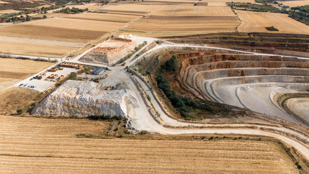 Aerial view of the open pit mine with terraced excavation piles of white stone and heavy machinery surrounded by agricultural fields in Besenovo Vojvodina Serbia. Aerial view of the open pit mine with terraced excavation piles of white stone and heavy machinery surrounded by agricultural fields in Besenovo Vojvodina Serbia.