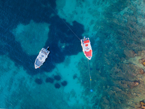 Aerial view of two small motorboats anchored in crystal clear turquoise water above a rocky seabed in Ksamil Vlore County Albania. Aerial view of two small motorboats anchored in crystal clear turquoise water above a rocky seabed in Ksamil Vlore County Albania.