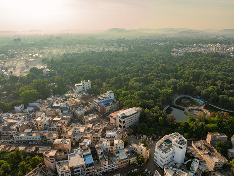Aerial view of the cityscape of Udaipur featuring dense residential buildings a lush green park and a small pond under a hazy sky during golden hour in Udaipur Rajasthan India.