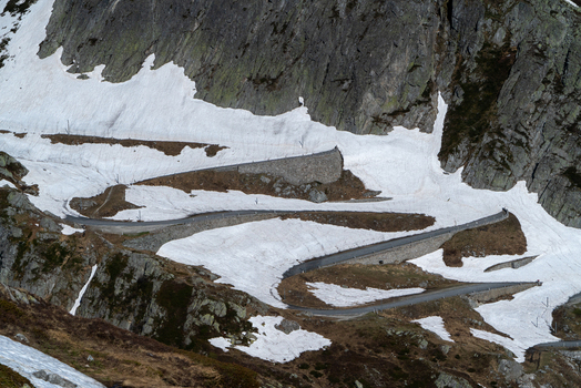 View of the winding Sankt Gotthard Pass road with its historic stone walls snaking through snow covered rocky slopes in Airolo Ticino Switzerland.