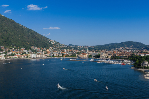 Aerial view of the city of Como nestled along the shores of Lake Como with boats on the water historic buildings and lush green mountains in Como Lombardy Italy.