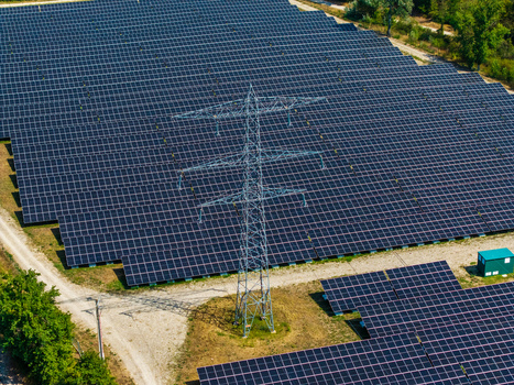 Aerial view of Solarfeld solar farm with rows of photovoltaic panels and a high voltage electricity pylon in Hombourg Grand Est France.