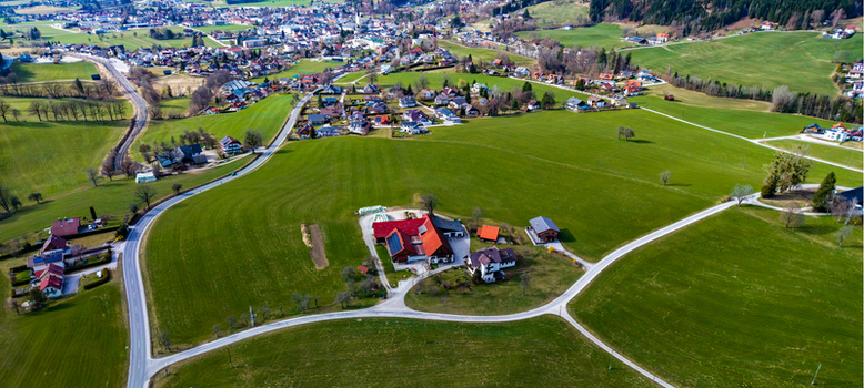 Aerial view of a quaint village nestled amidst rolling green hills where roads meander towards a cluster of houses with striking red roofs Windischgarsten Upper Austria Austria. Aerial view of a quaint village nestled amidst rolling green hills where roads meander towards a cluster of houses with striking red roofs Windischgarsten Upper Austria Austria.