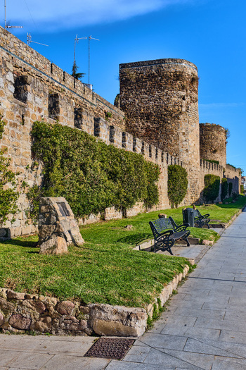 Plasencia Spain 03 December 2025 View of the medieval city walls with stone towers green hedges and park benches along a paved walkway under a clear blue sky. Plasencia Spain 03 December 2025 View of the medieval city walls with stone towers green hedges and park benches along a paved walkway under a clear blue sky.