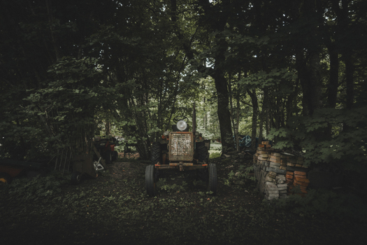 View of an old weathered tractor parked in a dense shaded forest with a stack of bricks nearby in Madise Harju County Estonia.
