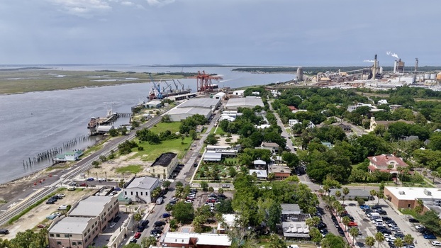 Aerial view of the port with red cranes and ships adjacent to green residential areas and a distant factory. Fernandina Beach Florida United States. Aerial view of the port with red cranes and ships adjacent to green residential areas and a distant factory. Fernandina Beach Florida United States.