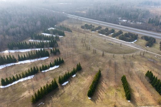 Aerial view of rows of evergreen trees and a semi circular path with patches of melting snow near a highway and misty forest in Lithuania.