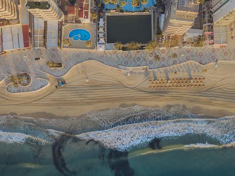 Aerial view of the sandy beach featuring a patterned promenade high rise buildings swimming pools and gentle waves rolling onto the shore in Calp Valencian Community Spain. Aerial view of the sandy beach featuring a patterned promenade high rise buildings swimming pools and gentle waves rolling onto the shore in Calp Valencian Community Spain.