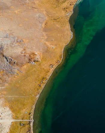 Aerial view of Sheosar Lake showing the contrast between the deep turquoise water and the dry golden brown landscape of the surrounding plains in Skardu Gilgit Pakistan.