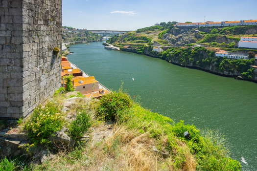 Aerial view of the Douro River snaking through the city bordered by ancient stone walls and lush greenery revealing the Dom Luís I Bridge in the distance Porto Porto District Portugal. Aerial view of the Douro River snaking through the city bordered by ancient stone walls and lush greenery revealing the Dom Luís I Bridge in the distance Porto Porto District Portugal.