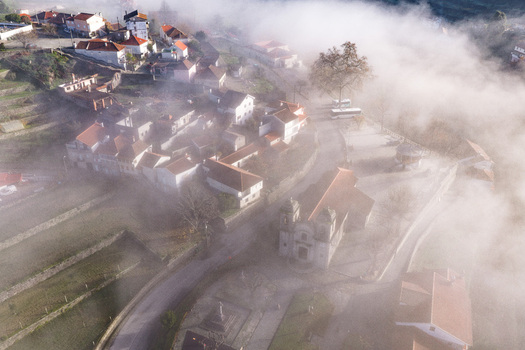 Aerial view of Avo village with red roofed houses and a historic church partially covered by thick morning fog in Oliveira do Hospital Coimbra District Portugal.
