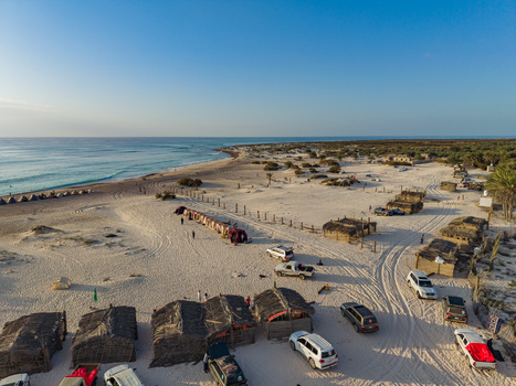 Aerial view of the contrasting thatched huts and parked cars dotting the sandy beach against the backdrop of the turquoise sea Kadrihnitin Socotra Yemen. Aerial view of the contrasting thatched huts and parked cars dotting the sandy beach against the backdrop of the turquoise sea Kadrihnitin Socotra Yemen.