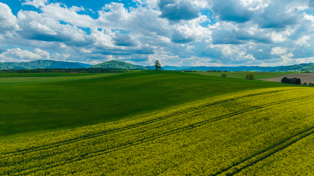 Aerial view of rolling green hills and vibrant yellow rapeseed fields under a cloudy blue sky with distant mountains Pribor Moravian Silesian Region Czechia. Aerial view of rolling green hills and vibrant yellow rapeseed fields under a cloudy blue sky with distant mountains Pribor Moravian Silesian Region Czechia.