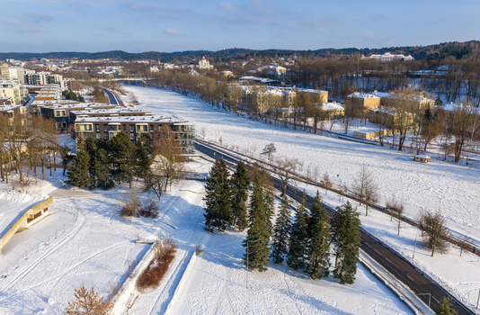 Aerial view of the frozen Neris River with snow covered banks modern residential buildings and evergreen trees in Lithuania. Aerial view of the frozen Neris River with snow covered banks modern residential buildings and evergreen trees in Lithuania.