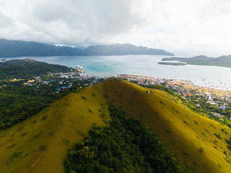 Aerial view of the lush grassy hills overlooking the coastal town and turquoise waters with boats Coron Mimaropa Philippines.