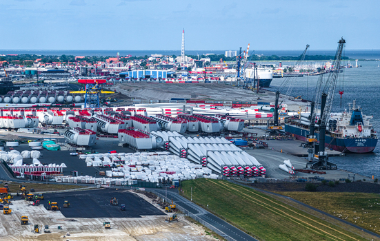 Aerial view of Siemens Gamesa Renewable Energy facility in the port of Cuxhaven featuring wind turbine blades nacelles industrial cranes cargo ships and city skyline Cuxhaven Niedersachsen Germany.