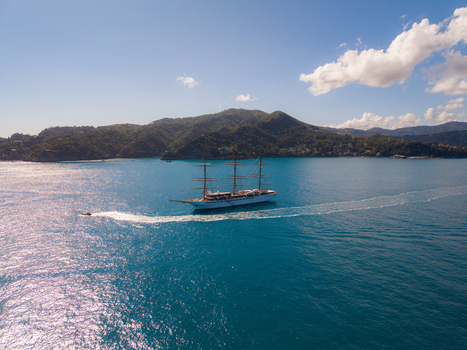 Aerial view of a large multi masted sailing ship cruising through the turquoise waters of the Mediterranean Sea near the lush green coastline of Portofino Liguria Italy. Aerial view of a large multi masted sailing ship cruising through the turquoise waters of the Mediterranean Sea near the lush green coastline of Portofino Liguria Italy.