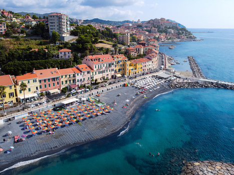 Aerial view of the coastal town featuring colorful buildings and a dark sand beach with orange umbrellas along the turquoise sea in Imperia Liguria Italy. Aerial view of the coastal town featuring colorful buildings and a dark sand beach with orange umbrellas along the turquoise sea in Imperia Liguria Italy.