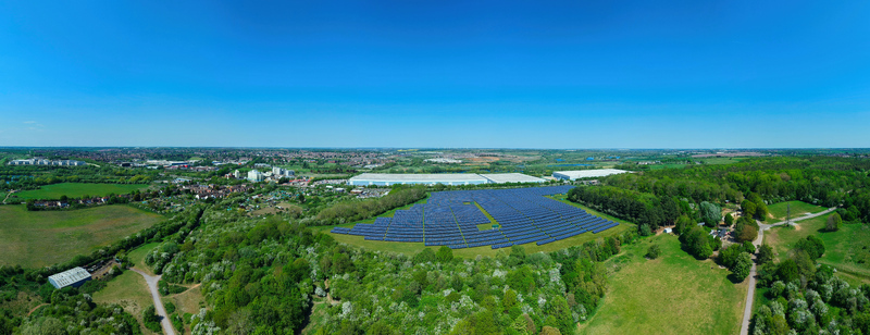 Aerial view of a large solar farm with rows of blue panels nestled among lush green trees and fields under a clear sky near Little Irchester England United Kingdom. Aerial view of a large solar farm with rows of blue panels nestled among lush green trees and fields under a clear sky near Little Irchester England United Kingdom.