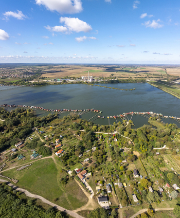 Aerial view of Bokodi Floating Village featuring wooden houses on stilts over the lake surrounded by green fields and a power plant in the distance in Oroszlany Hungary. Aerial view of Bokodi Floating Village featuring wooden houses on stilts over the lake surrounded by green fields and a power plant in the distance in Oroszlany Hungary.